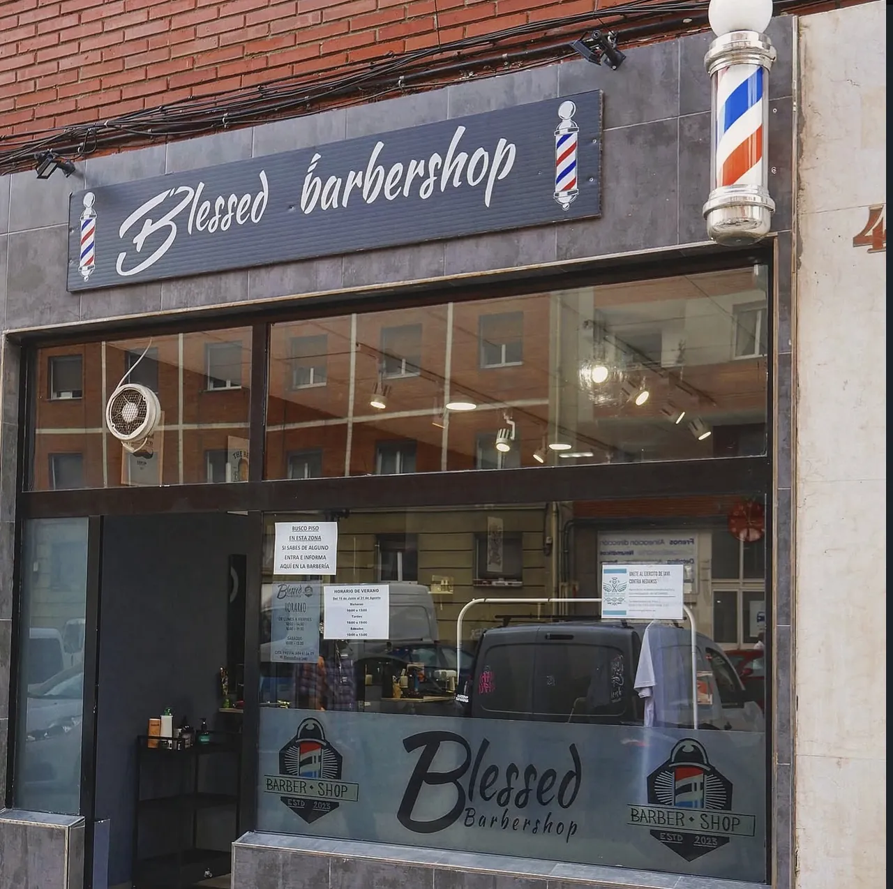 Fachada de Blessed Barbershop con el poste de barbero junto a la puerta
