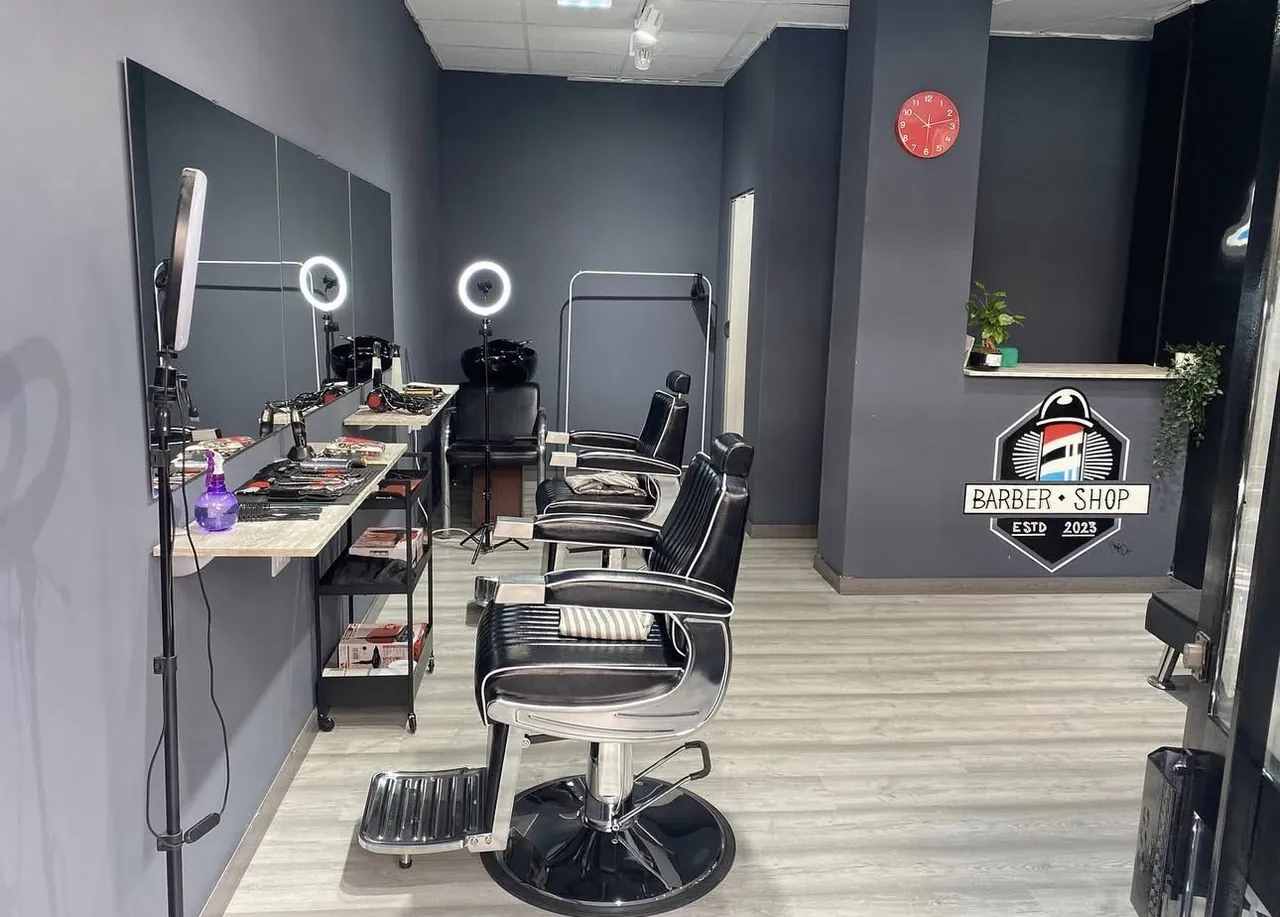 Interior de la barbería: dos sillones de barbero negros frente a un espejo con luces de aro